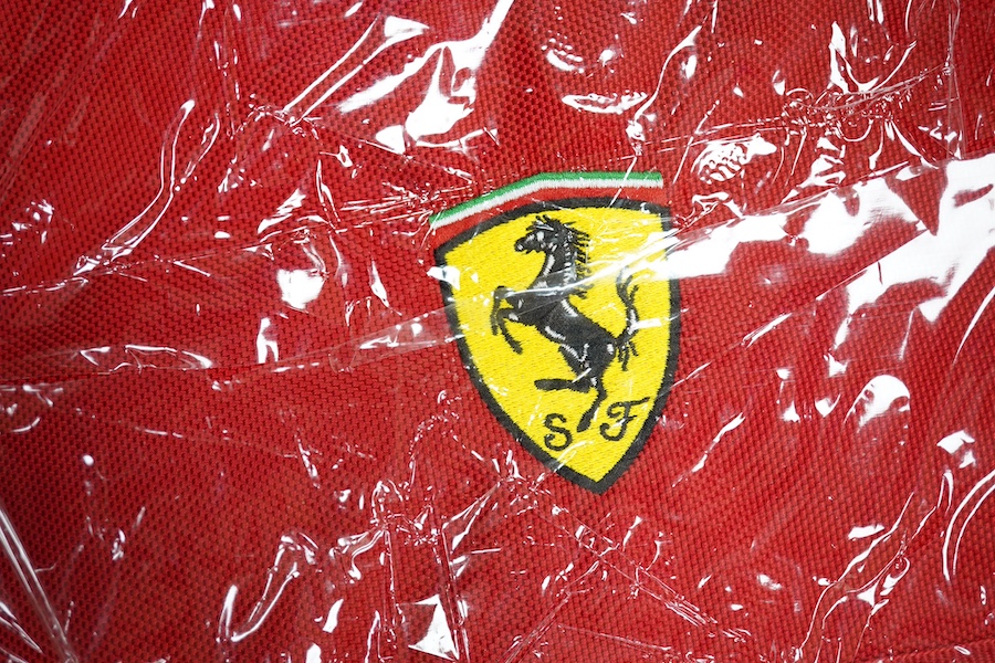 Two official Ferrari branded bags; a backpack and a duffle bag, both new with tags, both contained within an original Ferrari plastic bag dated 2002. Condition - good.